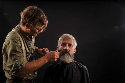 Barber cuts a beard to a client to an elderly gray-haired man Foto stock