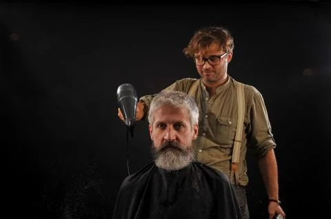 Barber cuts a beard to a client to an elderly gray-haired man Foto stock