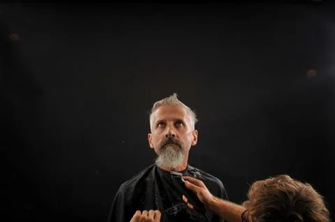 Barber cuts a beard to a client to an elderly gray-haired man Foto stock