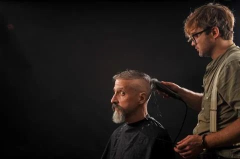Barber cuts a beard to a client to an elderly gray-haired man Foto stock