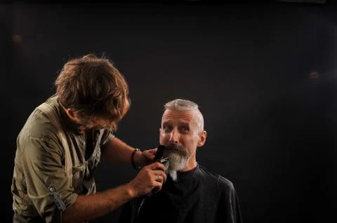 Barber cuts a beard to a client to an elderly gray-haired man Foto stock