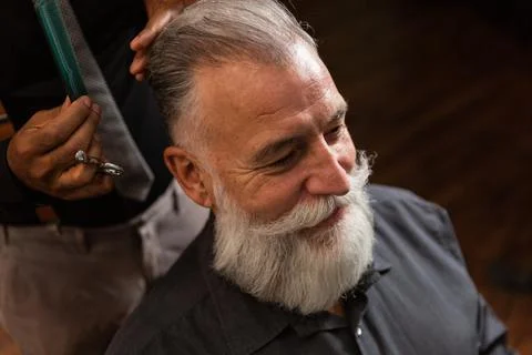 Barber cuts the beard to the customer with the scissors. Stock Photos