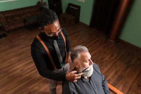 Barber cuts the beard to the customer with the scissors. Stock Photos