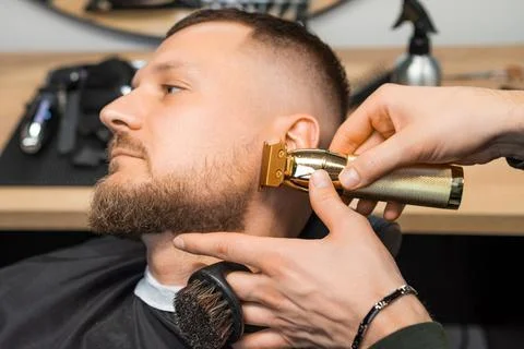 Barber cuts beard of man making stylish shape with trimmer Stock Photos