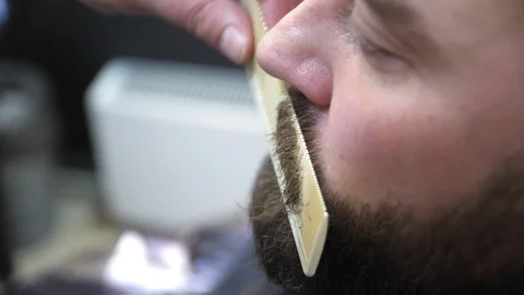 Barber cuts client beard with a professional beard trimmer in a barbershop on 動画素材 103449353