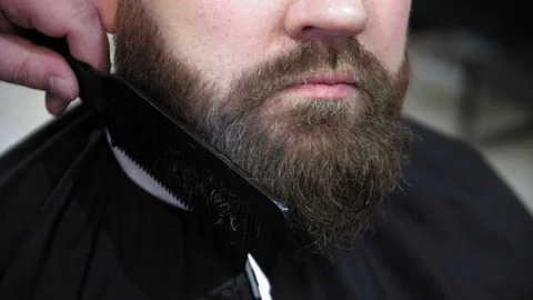 Barber cuts client beard with a professional beard trimmer in a barbershop Stock Footage 103449464