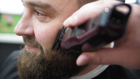 Barber cuts client beard with a professional beard trimmer in a barbershop on Stock Footage 103449491