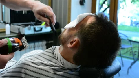 Barber cuts clients beard with a professional beard trimmer in a barbershop on Stock-Footage 90464948
