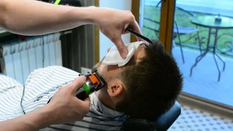 Barber cuts clients beard with a professional beard trimmer in a barbershop on Video stock 90465022