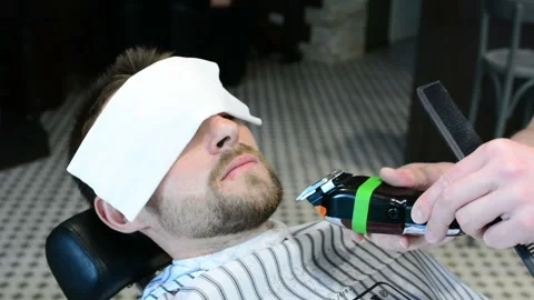 Barber cuts clients beard with a professional beard trimmer in a barbershop on Stock Footage 90465325