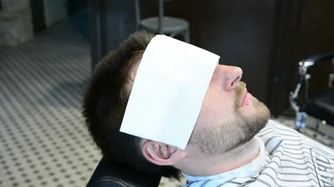 Barber cuts clients beard with a professional beard trimmer in a barbershop on Stock Footage 90465528