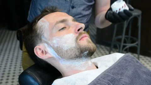 Barber cuts clients beard with a professional beard trimmer in a barbershop on Stock Footage 90466239