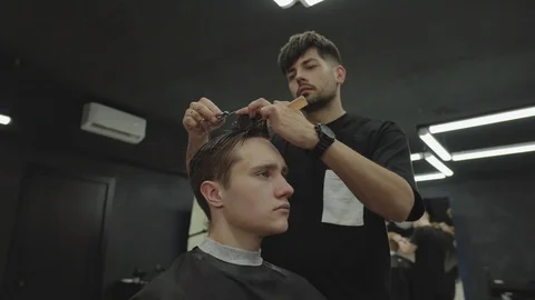 Barber cuts the hair of the client with scissors. Attractive male is getting a Vídeo Stock 112830919