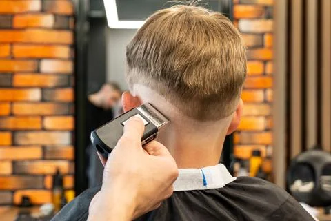Barber cuts red-haired client occiput with adjustable trimmer in barbershop Stock Photos
