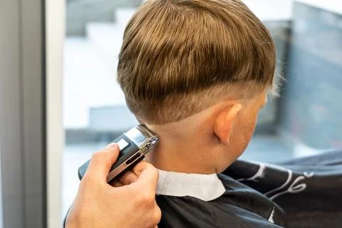 Barber cuts red-haired client occiput with adjustable trimmer in barbershop Stock Photos