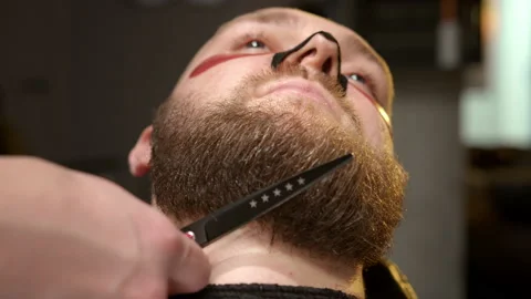 Barber is cutting beard of man using scissors in professional barbershop. Stock Footage 233464653