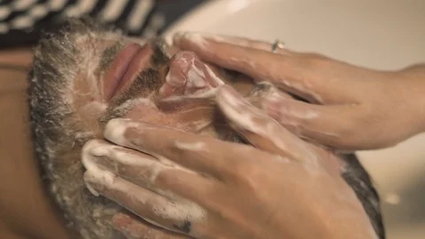 Barber doing face massage to bearded man in barbershop. Close up face washing Stock Footage 94643795