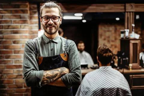 Barber man in an apron with arms crossed and happy in salon Stock Photos