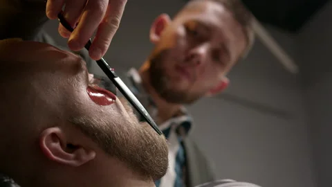 Barber man is cutting beard of client using scissors in professional barbershop. Stock Footage 232955139