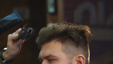 The Barber man in the process of drying a client's hair with a Hairdryer at the Stock Footage 70951398