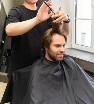A barber, with scissors and a comb, is giving a haircut to a male client Fotos Stock