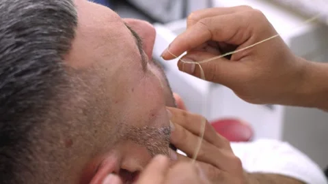 Barber shaping eyebrows with thread on young man precise grooming Stock Footage 333195802