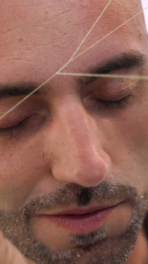 Barber shaping eyebrows with thread on young man precise grooming 스톡 동영상 333199895