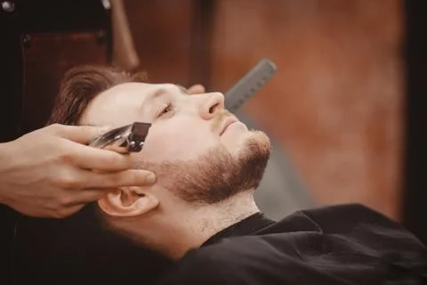 Barber shaves beard of client man on chair Barbershop 写真素材