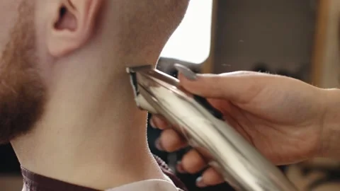 Barber shaves with an electric razor to a man in a barber shop Stock Footage
