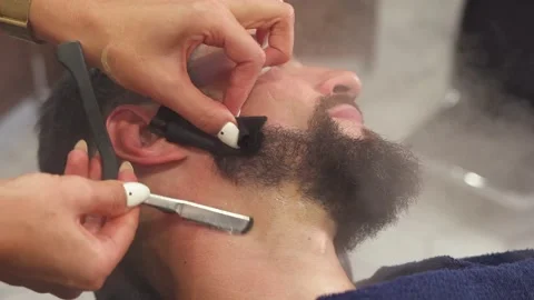 Barber shaving bearded man with sharp razor in Barber shop. Bearded male sitting Stock Footage 159879730