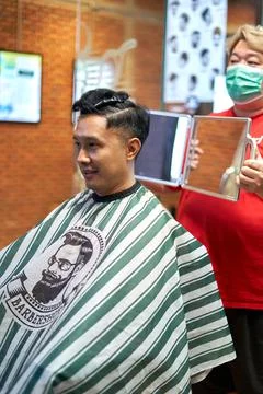 Barber showing the haircut of a client using a mirror in a barber shop Stock Photos