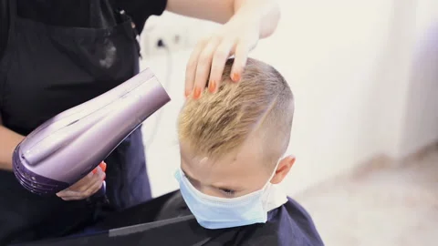 Barber styling his little client hair using a hairdryer. Hairdressing during the Stock Footage 136876176