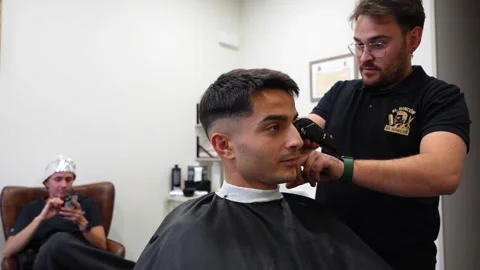 Barber talking with customer while another client waits under silver foil for Stock Footage 322514105