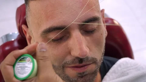 Barber threading eyebrows shaping clean lines on young man 库存影片 333195834