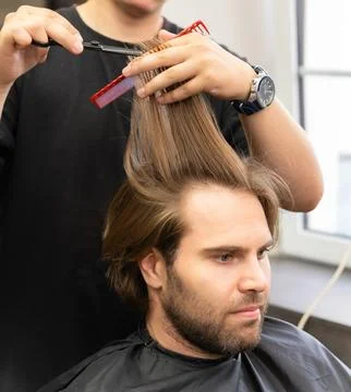 A barber uses scissors and a red comb to style a male client's long hair. Stock Photos