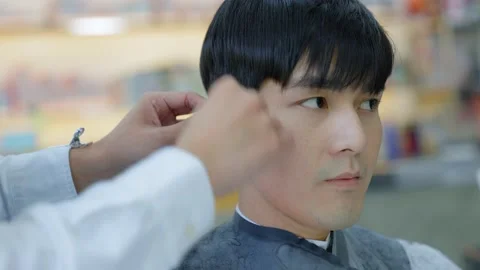 The barber is using a brush to remove the hair from the customer's ear after  Stock Footage 153953630