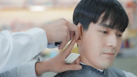 The barber is using a clipper to cut the ear area for the customer. Professio 스톡 동영상 153953661