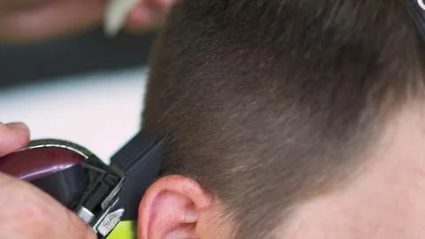 Barber using clippers to cut a young man's hair Stock Photos