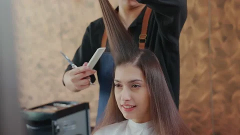 The barber is using scissors to trim the ends of the hair to a beautiful youn Stock Footage 153959911
