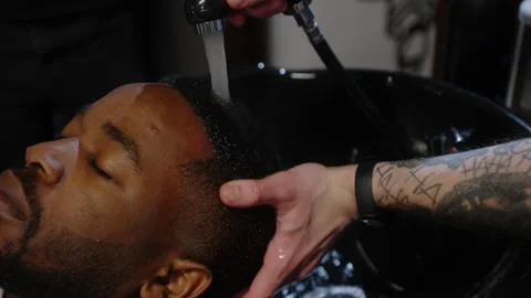 Barber washes shampoo off the head of an African American in a special sink Stock Footage