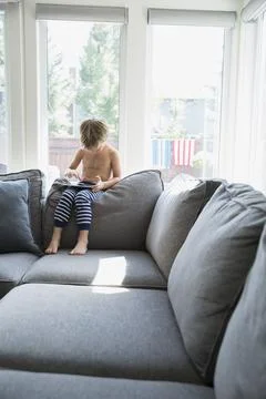 Bare chested boy in pajamas using digital tablet on living room sofa Stock Photos