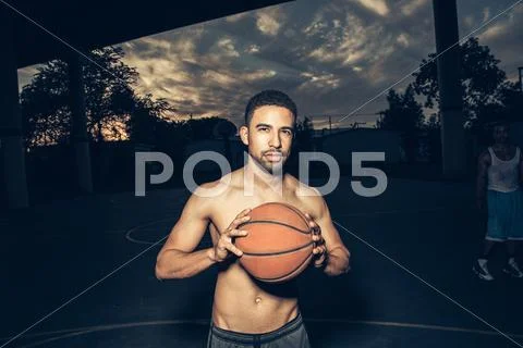 Bare Chested Man On Basketball Court Holding Basketball Looking At Camera