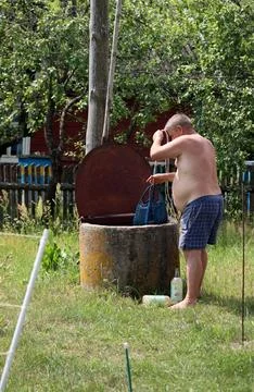 A bare-chested man in shorts pulls a string bag from the well. 写真素材