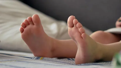 The bare feet of a child sitting in bed in the morning with a smartphone, watchi Video stock 261298413