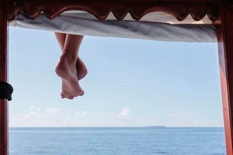 Bare feet hanging from dock over sunny ocean, Maldives Stock Photos