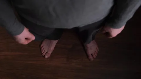 Bare feet of a man in gray clothes standing on the floor, top view Stock Footage 273685484