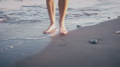 Bare feet of a man walking on a sandy sea beach with long waves at a resort Stock Footage 304846360