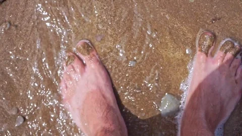 Bare feet on the shore of the beach as a wave gently covers the sand. Stock Footage 317163680