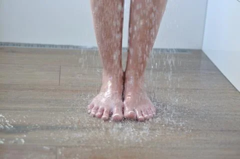 Bare feet standing under running water in the shower on a tiled bathroom floo Stock Photos