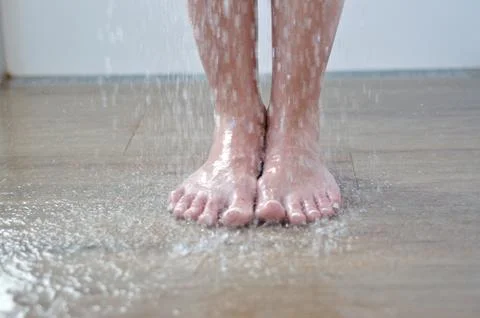 Bare feet standing under running water in the shower on a tiled bathroom floor Stock Photos